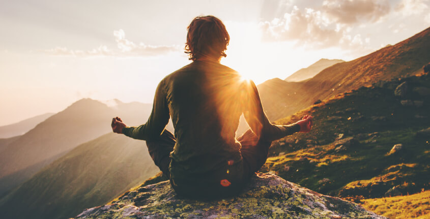 Homem meditando em cima de uma montanha